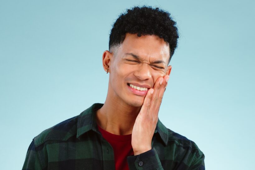 Young adult experiencing jaw pain and facial discomfort, a common symptom of TMJ disorder, often treated with professional TMJ therapy.